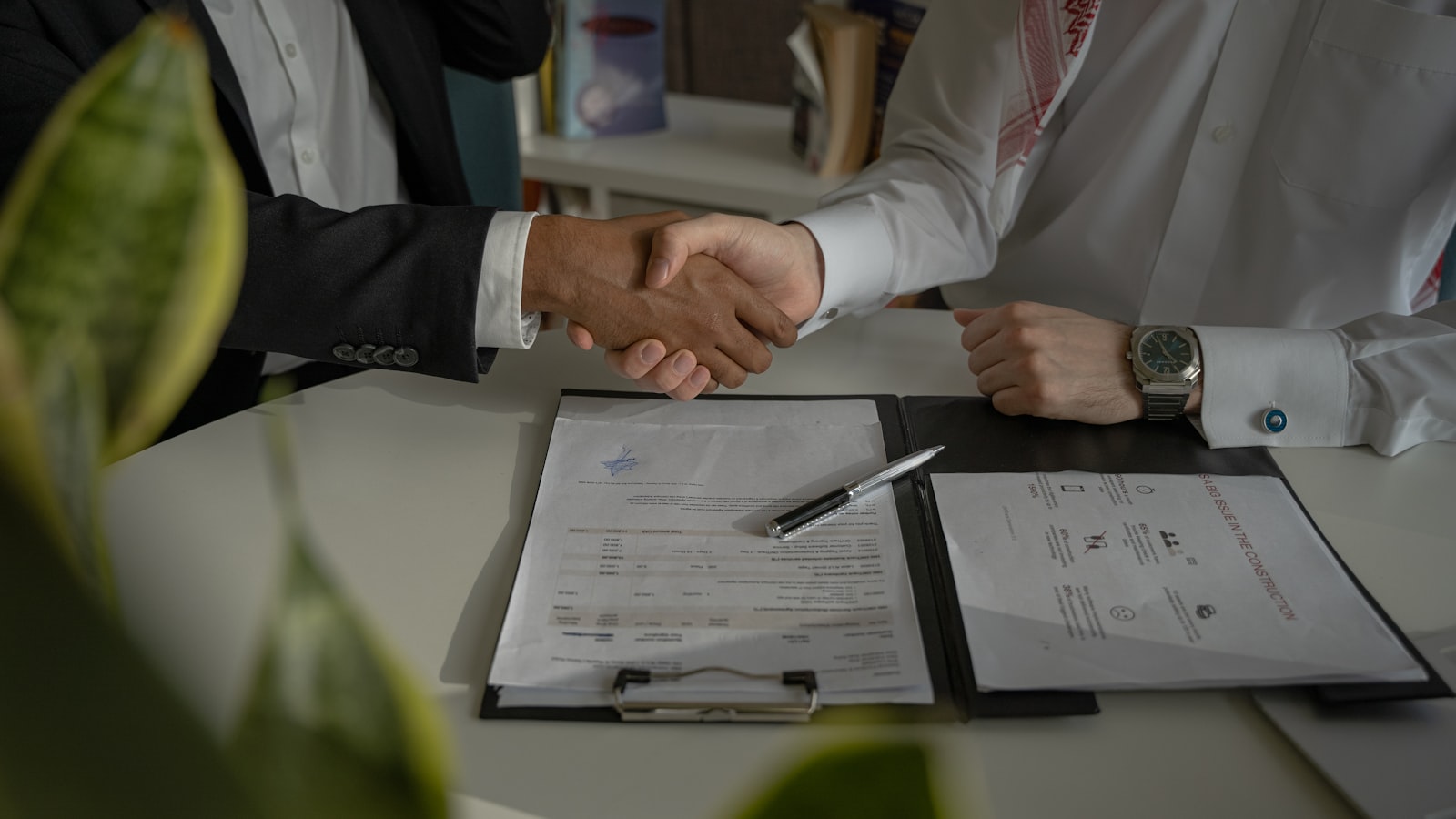 Two people shaking hands across a table over a paper agreement — closing a deal.
